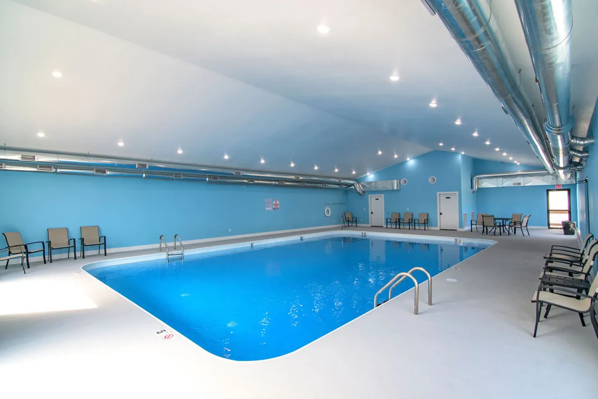 An inviting indoor swimming pool with tranquil blue walls, several reclining lounge chairs line the poolside, and the space is softly lit, suggesting a relaxing environment suitable for year-round use.