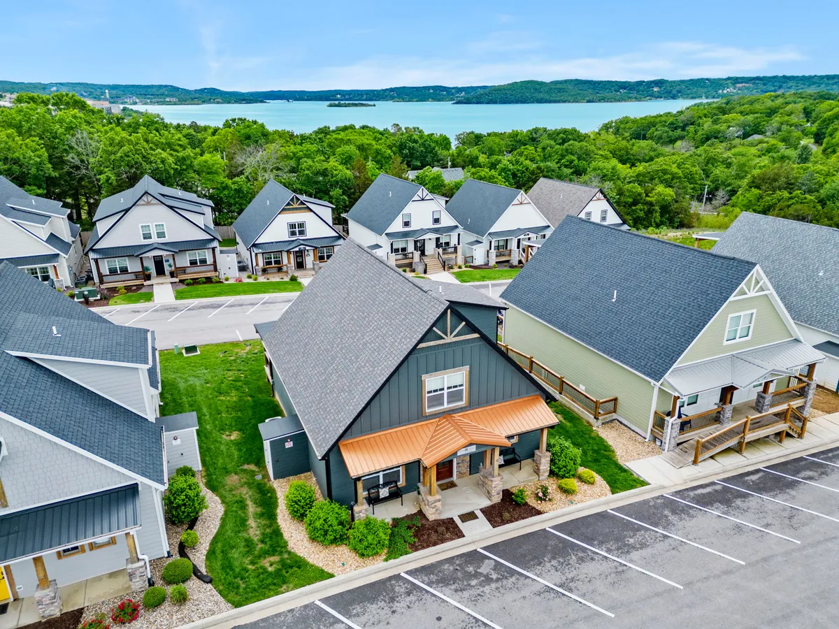 This image captures a welcoming lakefront house with a vibrant orange roof set amid lush green landscaping, and the serene waters of Table Rock Lake visible nearby. The spacious lawn and proximity to the water evoke the feeling of family-friendly outdoor activities such as picnics, barbecues, and lakeside gatherings.