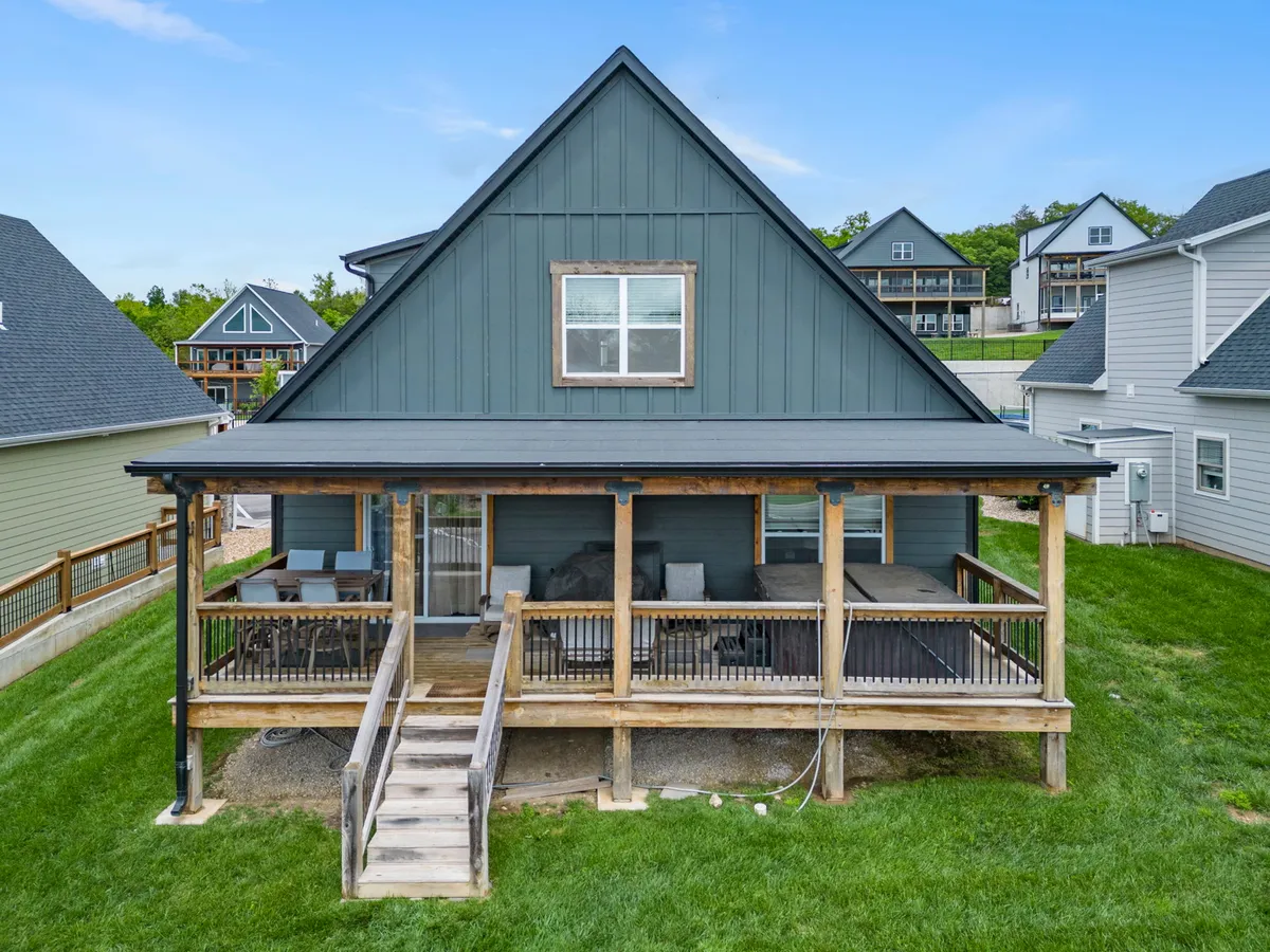 This image features a large porch with an inviting A-frame roof and green siding, surrounded by natural greenery. The space is set up for outdoor relaxation and social gatherings, hinting at opportunities for al fresco dining and morning coffee in nature.