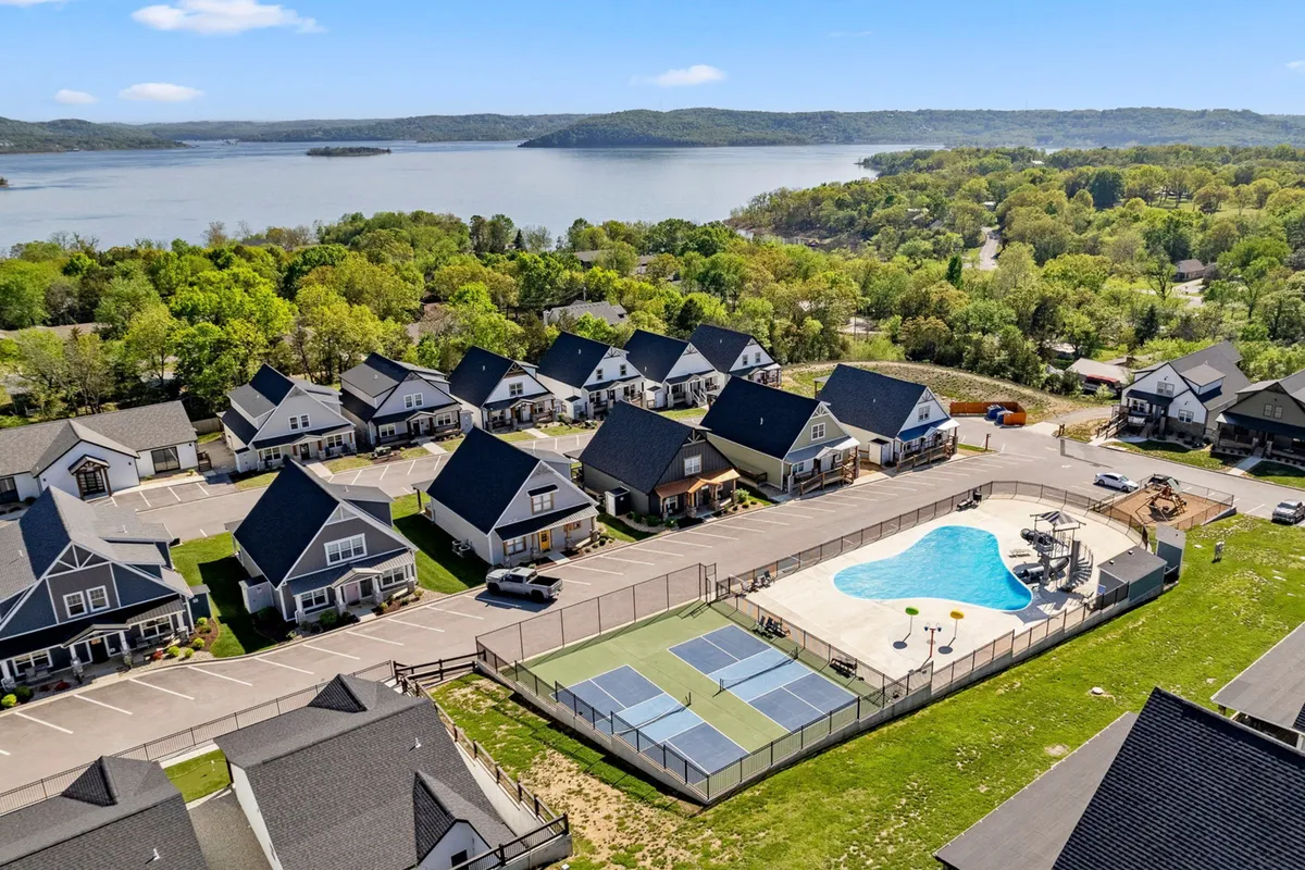 This exterior scene captures a vibrant communal area featuring a swimming pool, tennis courts, and a backdrop of residential buildings. The space is lively, with opportunities for swimming, playing tennis, relaxing by the pool, and enjoying lake views.