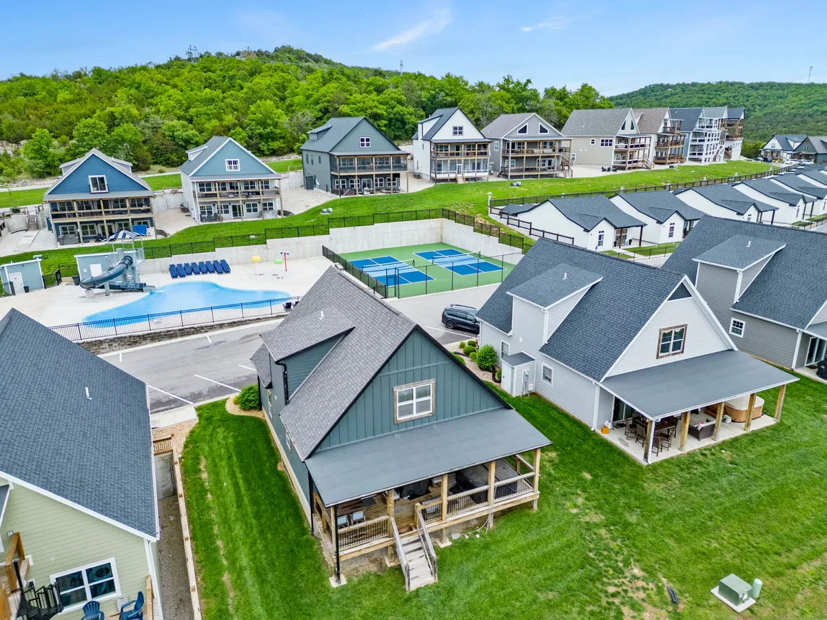 This exterior image shows a community space with a swimming pool, tennis/pickleball courts, expansive green lawns, and modern homes in the background. There are clear signs of outdoor activity and communal fun, reflecting both sports and relaxation.