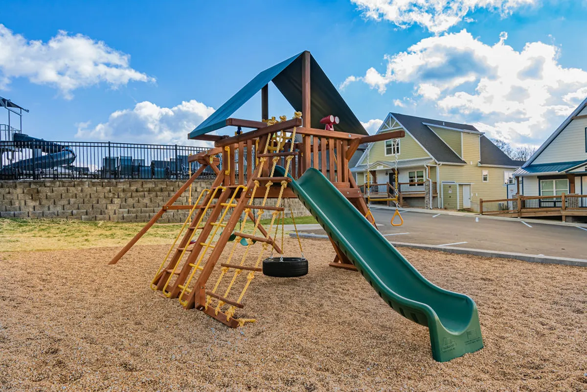 A cheerful playground scene featuring colorful equipment, including a slide, sandbox, and swing set. Children are seen laughing and playing, while families gather nearby for picnics, capturing the playful and communal spirit of the community.