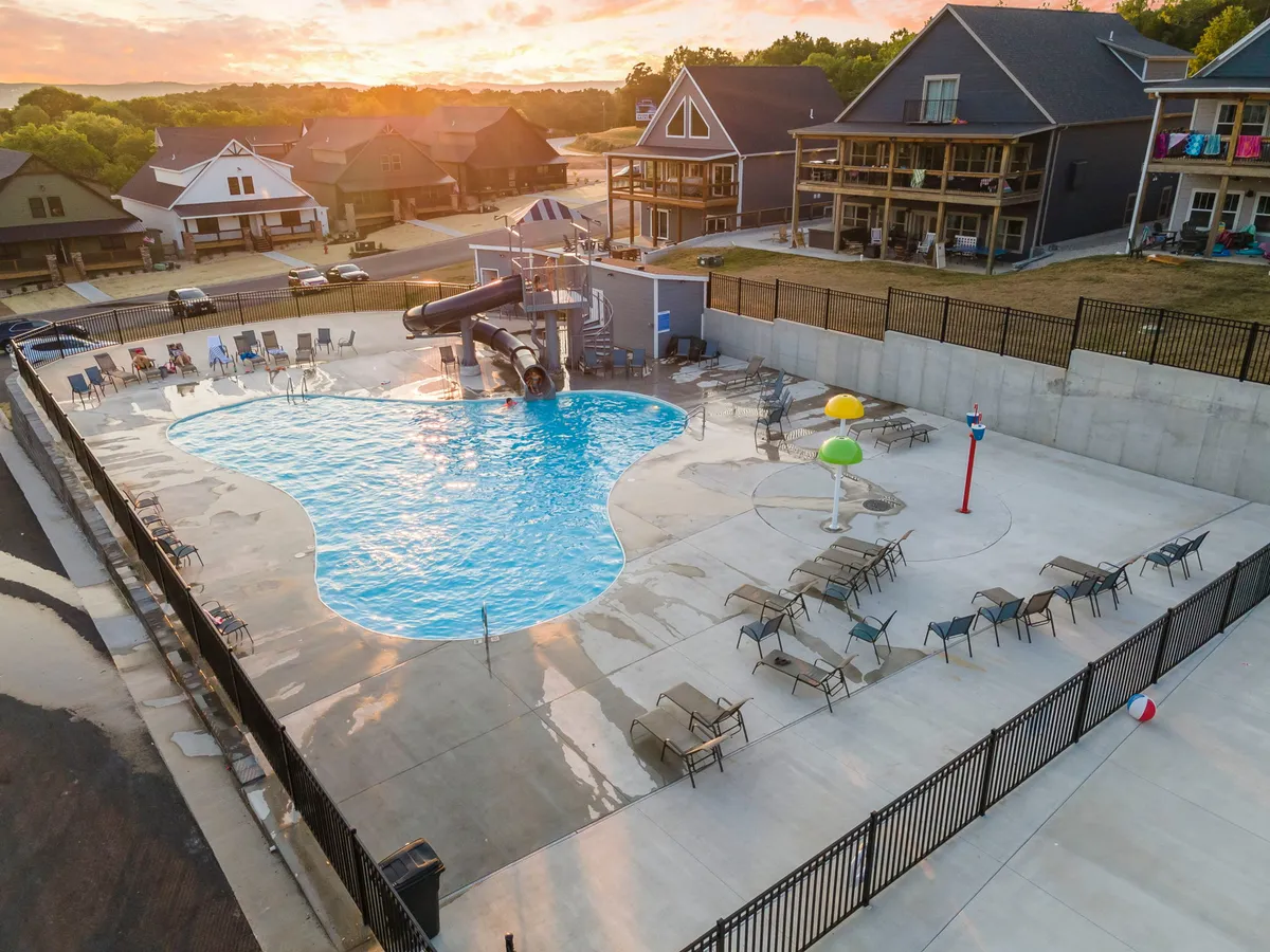 This vibrant exterior image displays a sparkling outdoor swimming pool complete with a thrilling water slide, surrounded by lounge chairs and colorful water features. Children and families are visible enjoying the pool, exuding a joyful and playful atmosphere ideal for summer fun.