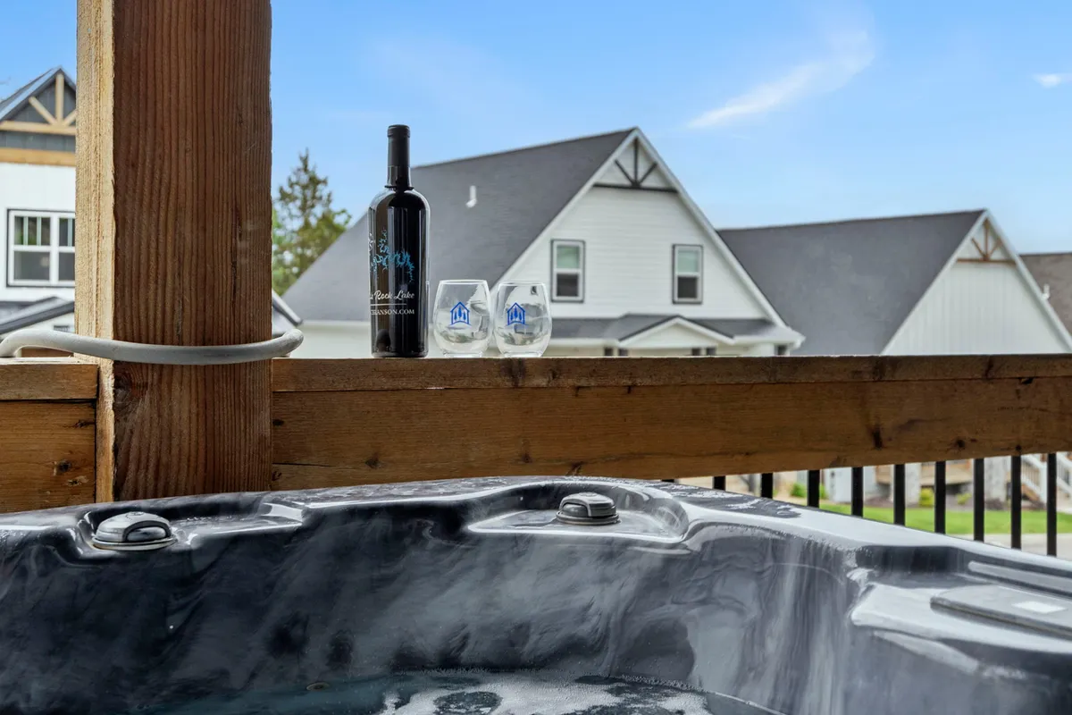 An inviting hot tub set on the deck, accompanied by a wine bottle and glasses—suggesting socializing or a romantic evening. Subtle hints of sunset create a warm, relaxing ambiance ideal for unwinding after a day of activities.