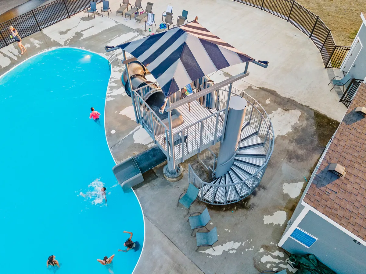 This image features a vibrant outdoor swimming pool area with a thrilling water slide and spacious seating around the pool. The scene is lively and energetic, capturing the fun and excitement of summer days spent swimming and socializing.
