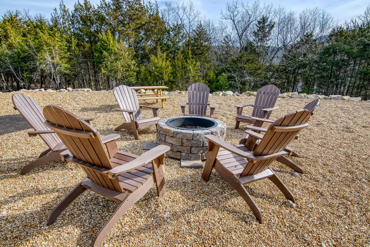 This cozy exterior scene centers on a fire pit surrounded by Adirondack chairs with trees in the background, evoking an atmosphere of togetherness, storytelling, and stargazing under the night sky.