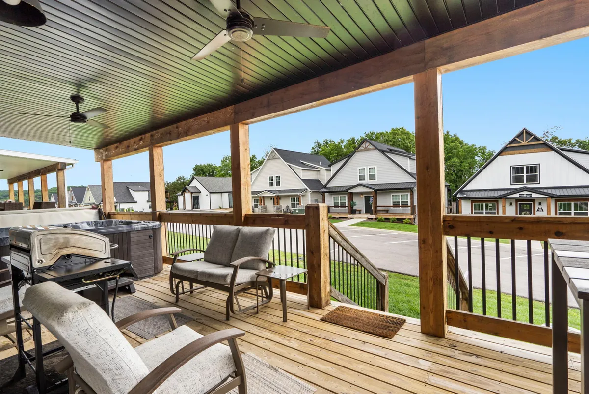 A wooden deck outfitted with a comfortable seating area and an outdoor grill, overlooking neighboring houses. The setup is perfect for outdoor dining, lounging, and hosting summer barbecues as the sun sets.
