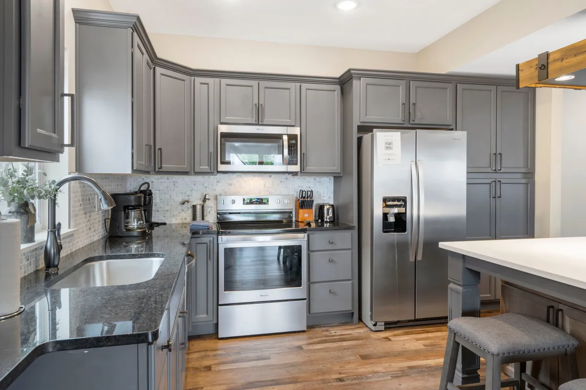 A modern, open kitchen with stainless steel appliances, dark granite countertops, and grey cabinetry. The layout invites group cooking and family interaction, with wide counters for meal prep and an open line of sight to communal areas.
