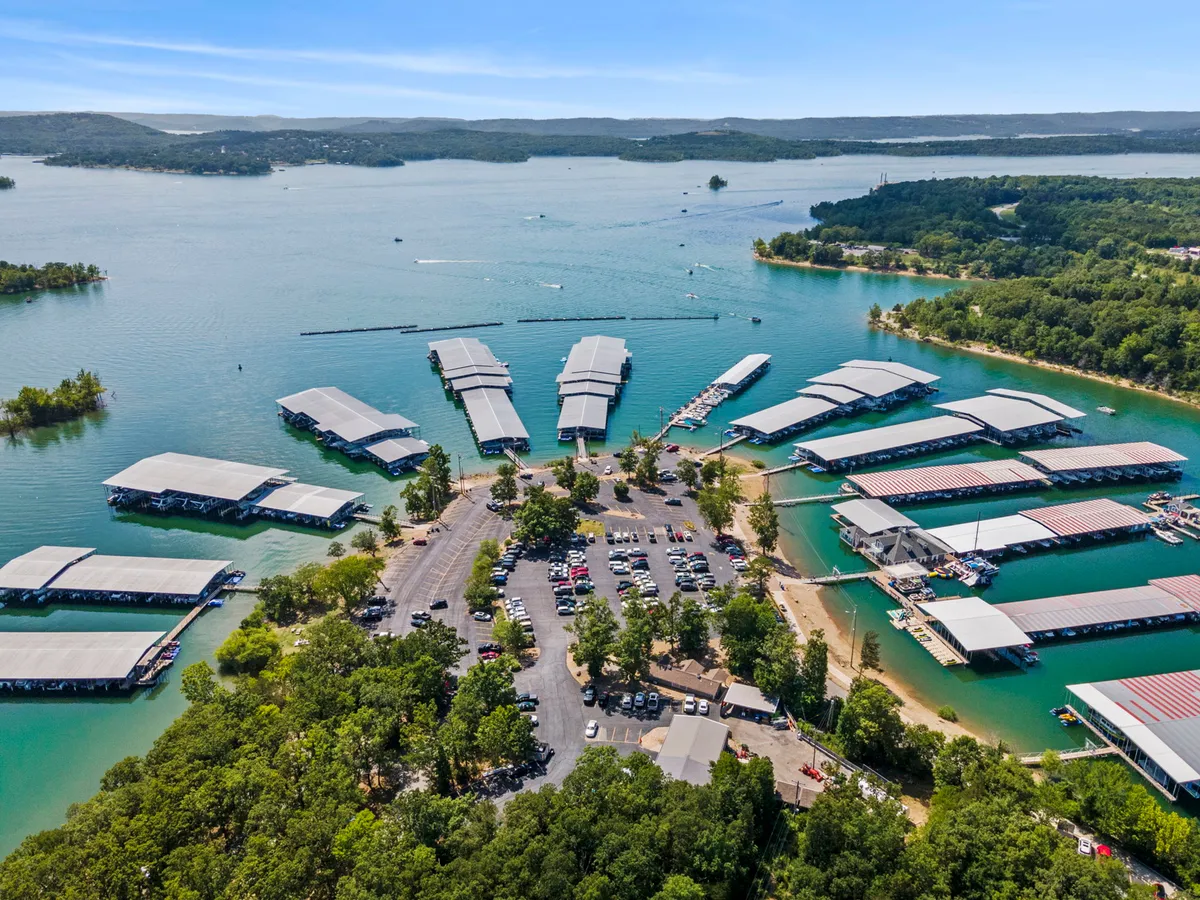 A panoramic view of the marina docks with boats moored along the water, surrounded by lush greenery and a nearby parking area. The lively yet peaceful waterfront setting invites guests to enjoy boating and water sports.