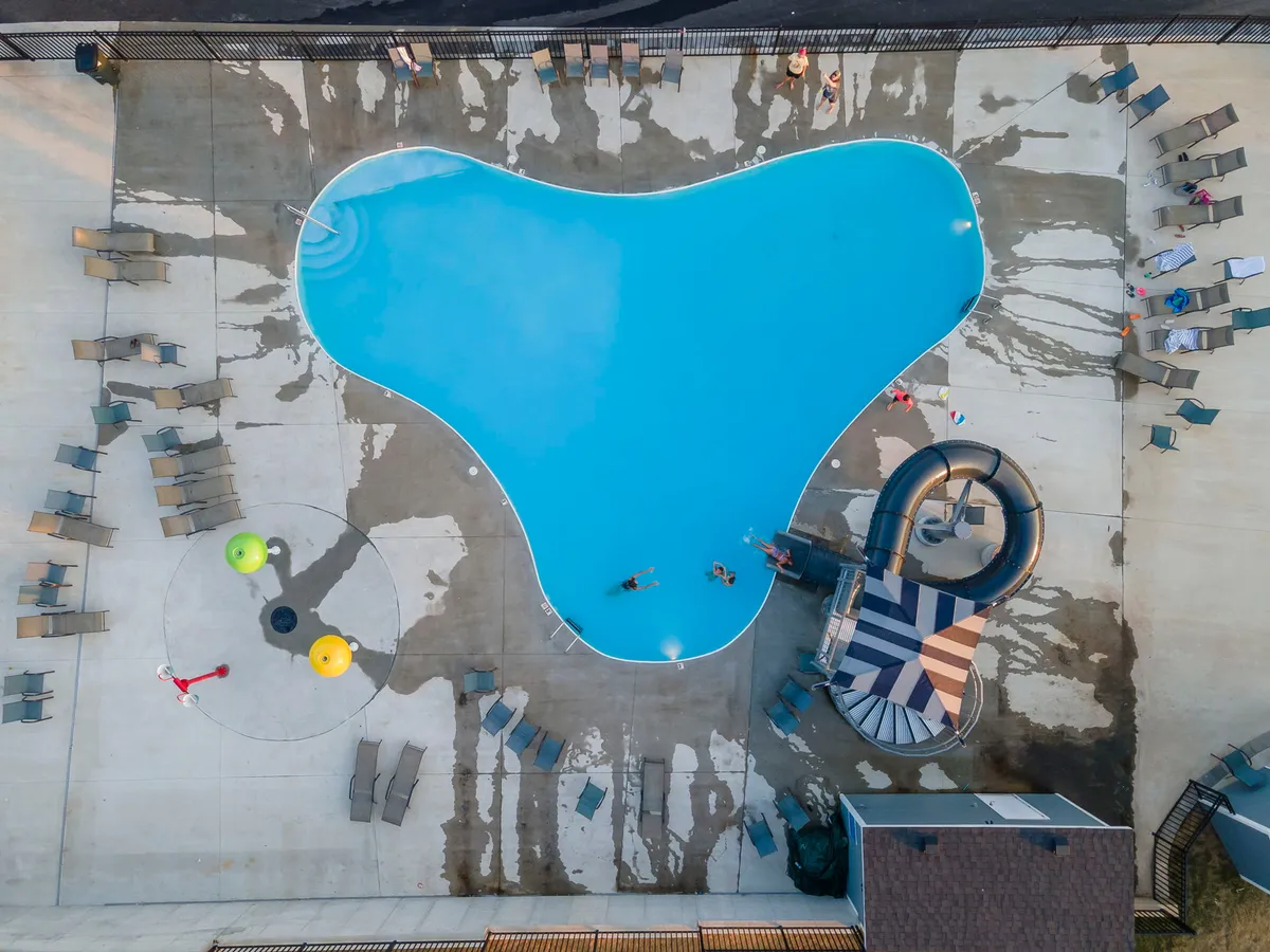 A vibrant outdoor pool area featuring a shaped swimming pool, an exciting water slide, colorful pool toys, and comfortable lounge chairs. The scene is filled with sunshine and playful energy, ideal for families and children.