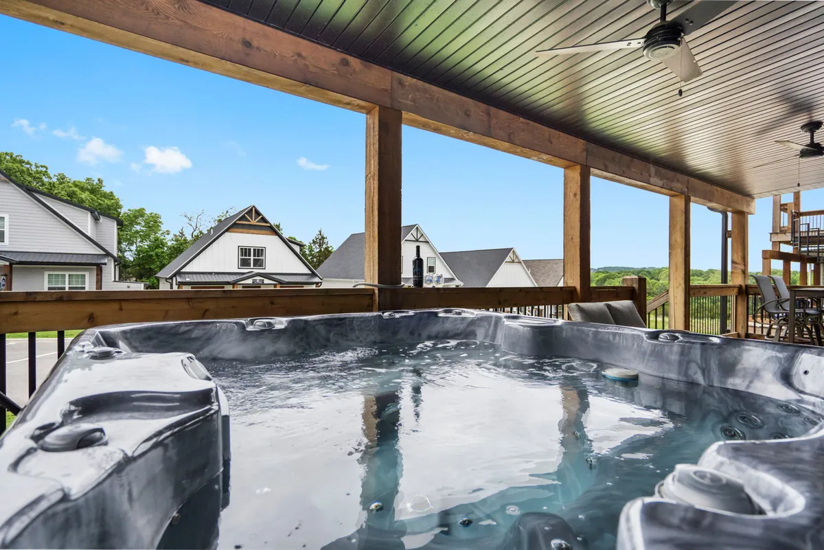 A tranquil view of the outdoor deck featuring a private hot tub, with a backdrop of blue skies and distant houses. The spacious deck invites relaxation, socializing, and soaking in the scenic surroundings.