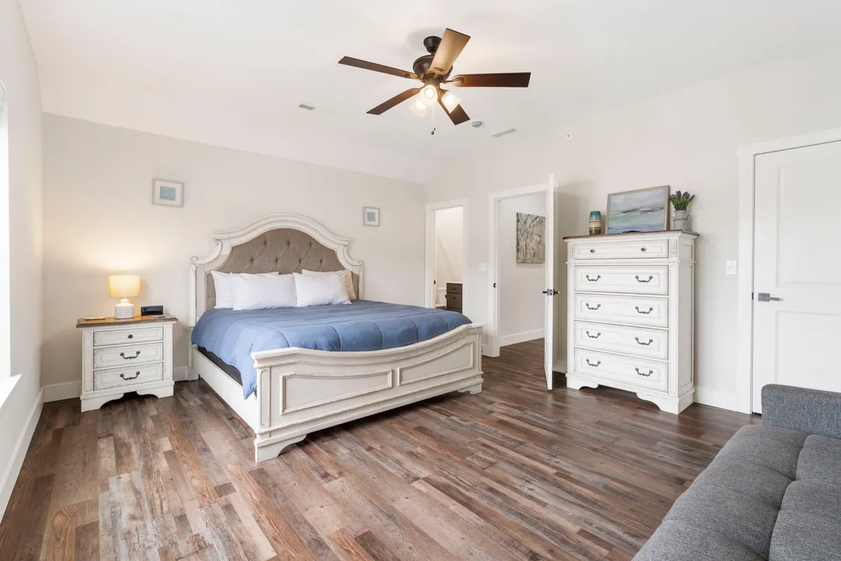 A serene bedroom featuring a comfortable bed, a dressing table, a dresser, and a window allowing in soft natural light. The decor is calming and the space is uncluttered, inviting guests to relax, read, or rest.