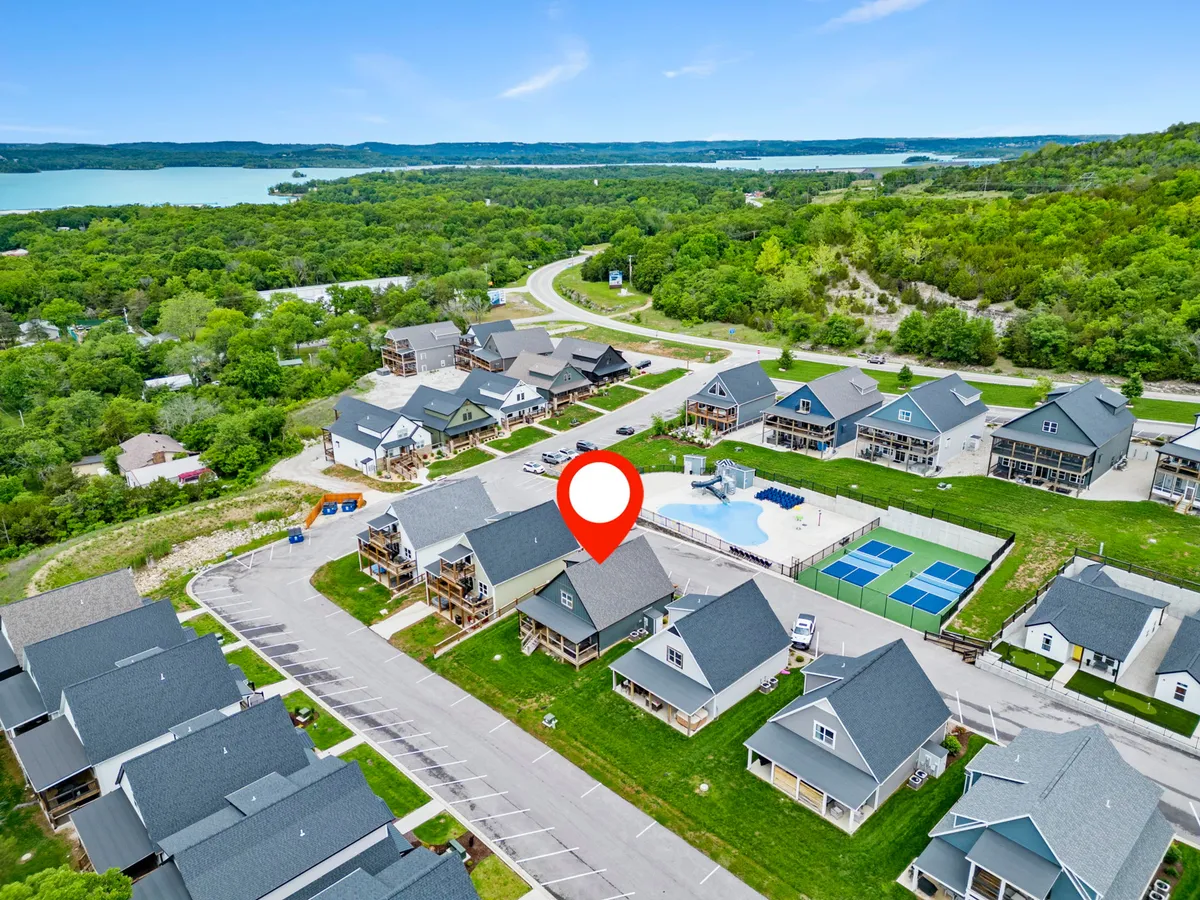 An expansive exterior shot showcasing a sparkling swimming pool and tennis courts surrounded by lush greenery and neighboring houses. The communal layout indicates resort-style amenities available to guests, including opportunities for swimming, tennis, and socializing outdoors.