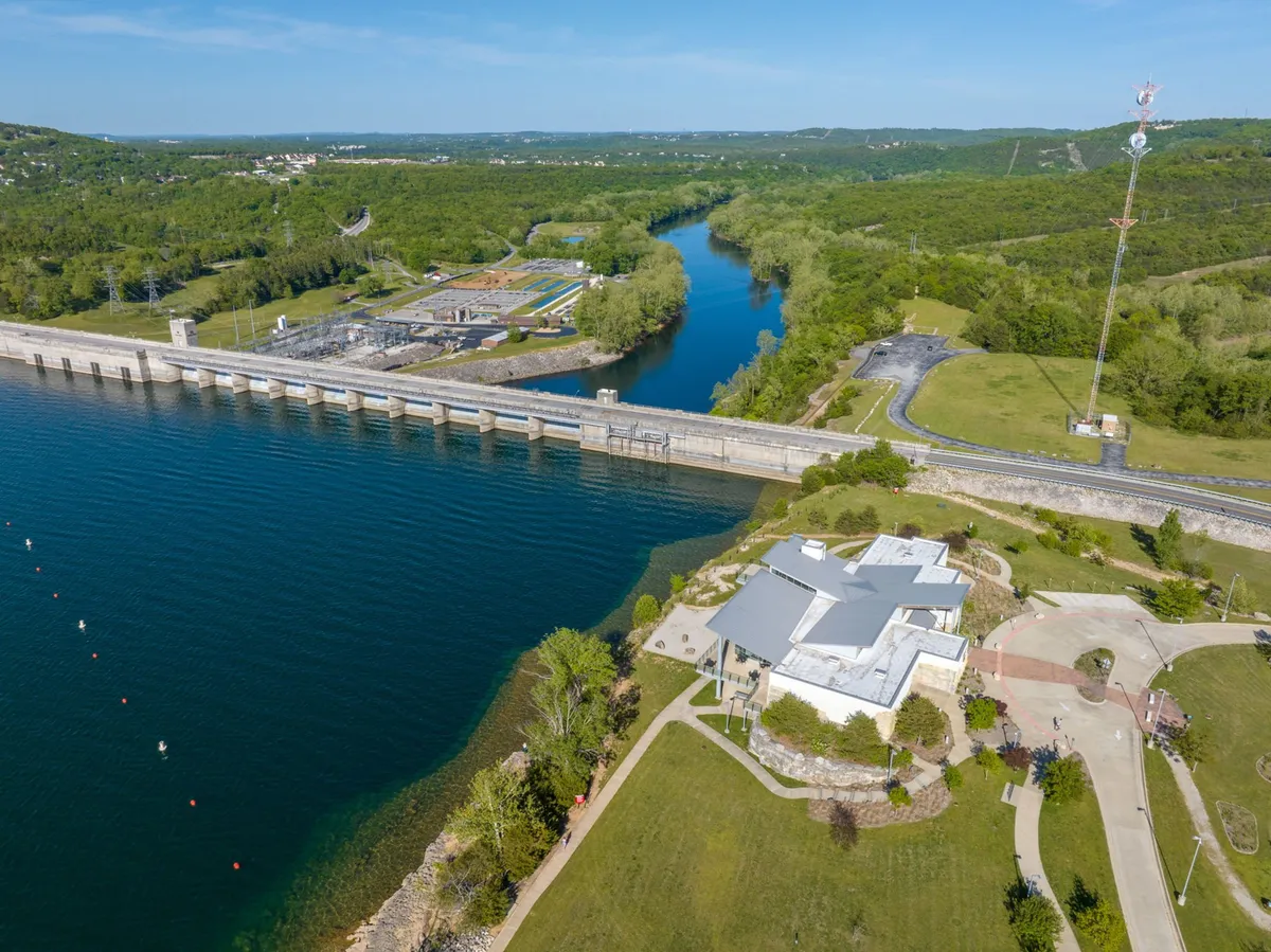A scenic exterior view featuring a serene water body bordered by greenery, a prominent dam, and a building nestled within the landscape. The area invites boating, fishing, and peaceful strolls, set against a beautiful sunset backdrop.